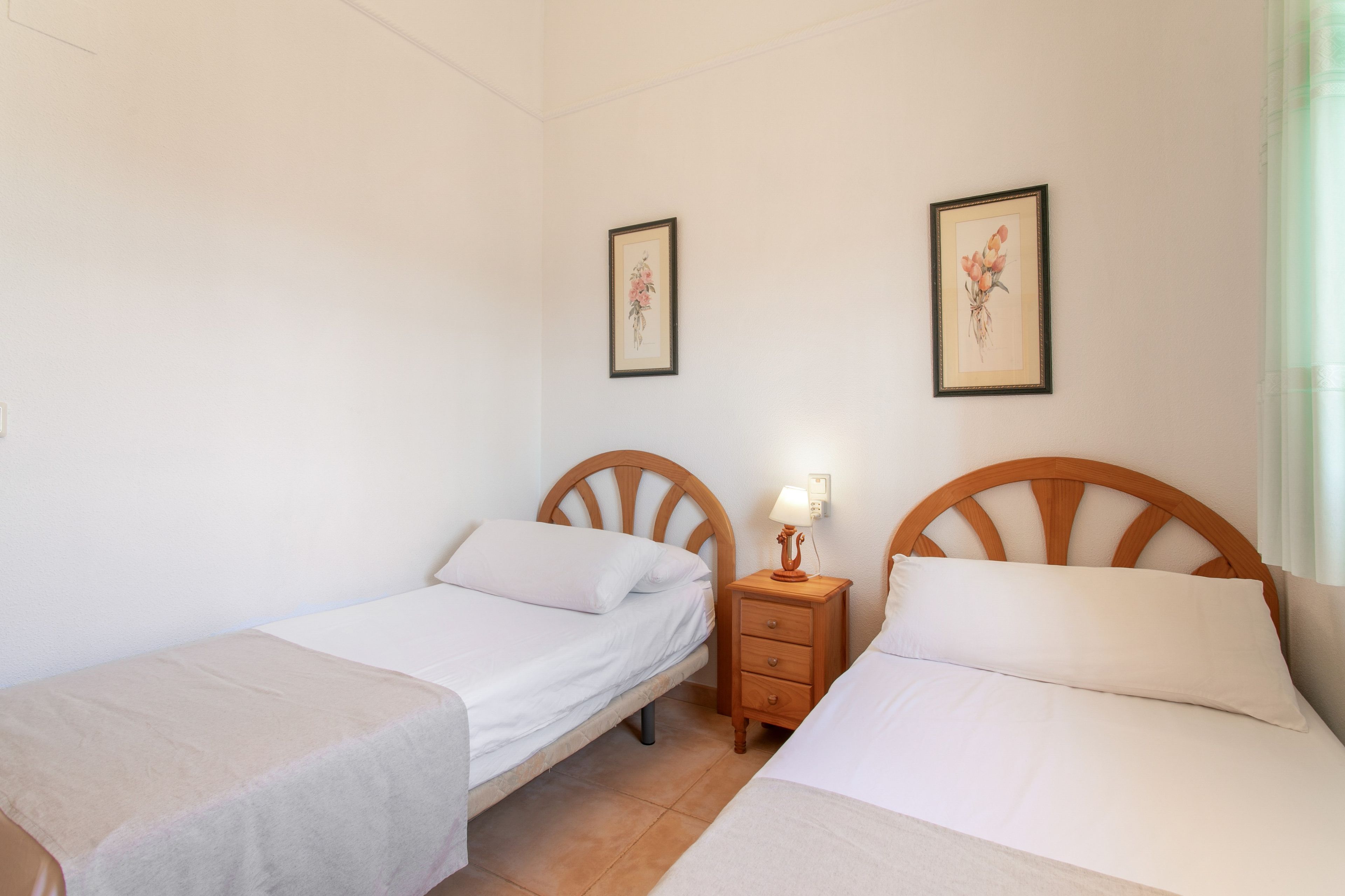 Een kamer met twee eenpersoonsbedden, elk met een houten hoofdeinde, een nachtkastje met een lamp en een lijst met een afbeelding aan de muur.