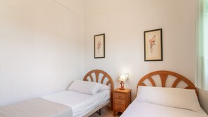 Ein Zimmer mit zwei Einzelbetten, jeweils mit einem Holzkopfstück, einem Nachttisch mit Lampe und einem gerahmten Bild an der Wand.