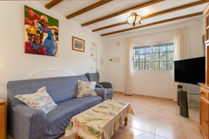 A living room with a sofa, a television, and a painting on the wall. - Bungalow 'Magnifico Chalet Con Piscina' with Shared Pool, Wi-Fi and Air Conditioning (Gran Alacant)