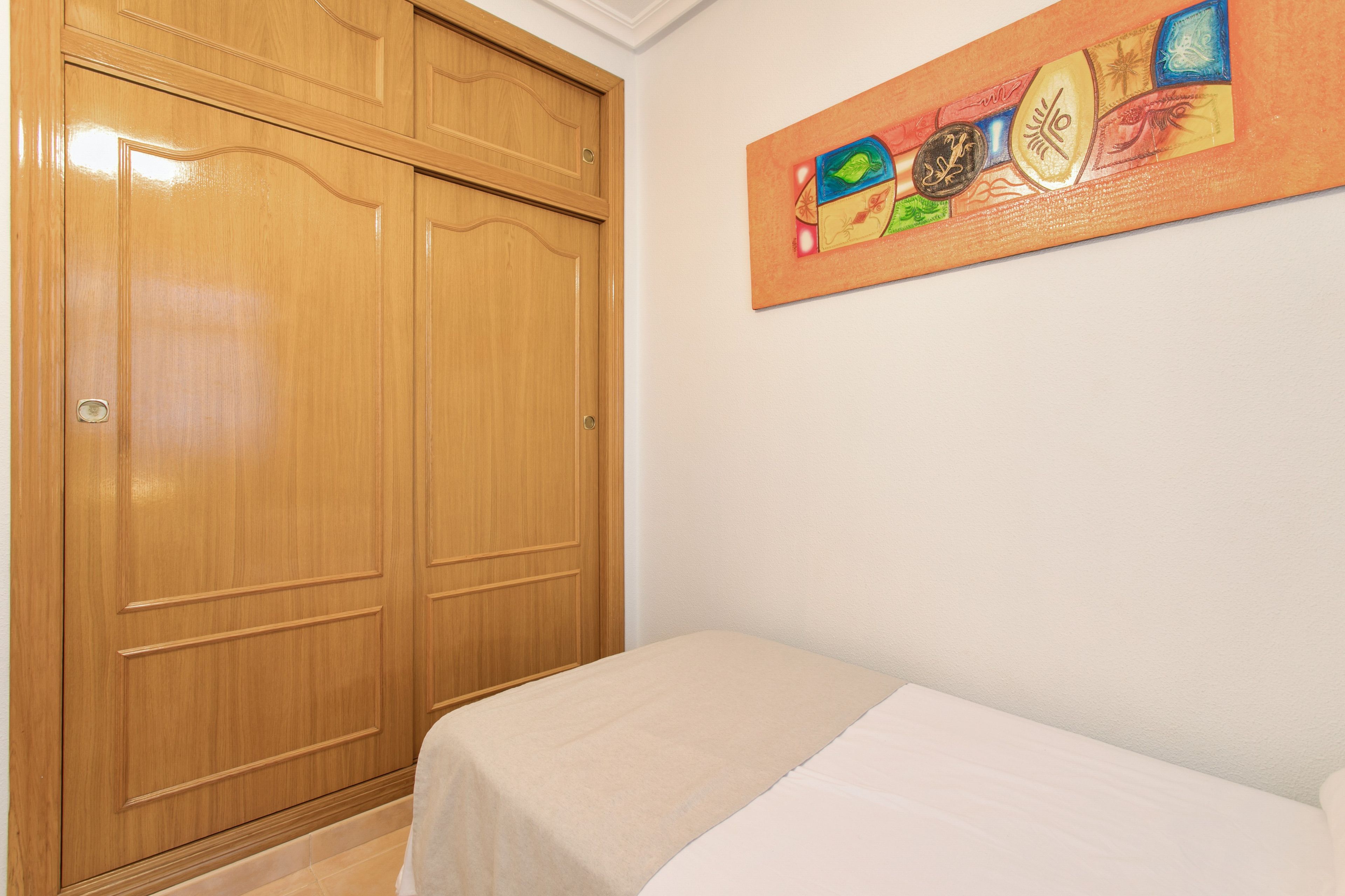 A room with a wooden wardrobe and a bed with a beige bedspread.