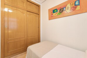 Una habitación con un armario de madera y una cama con colcha color beige.