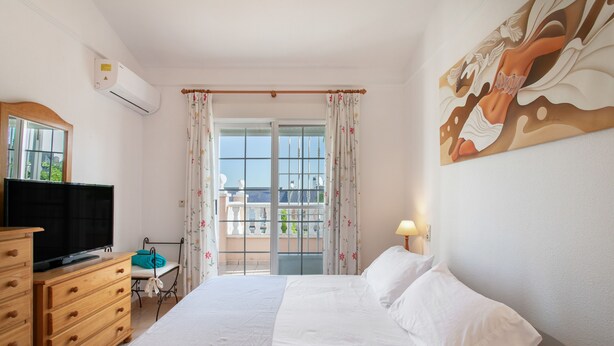 Ein Hotelzimmer mit Bett, Schminktisch, Fernseher, einem Balkon mit Aussicht und einem Bild an der Wand.