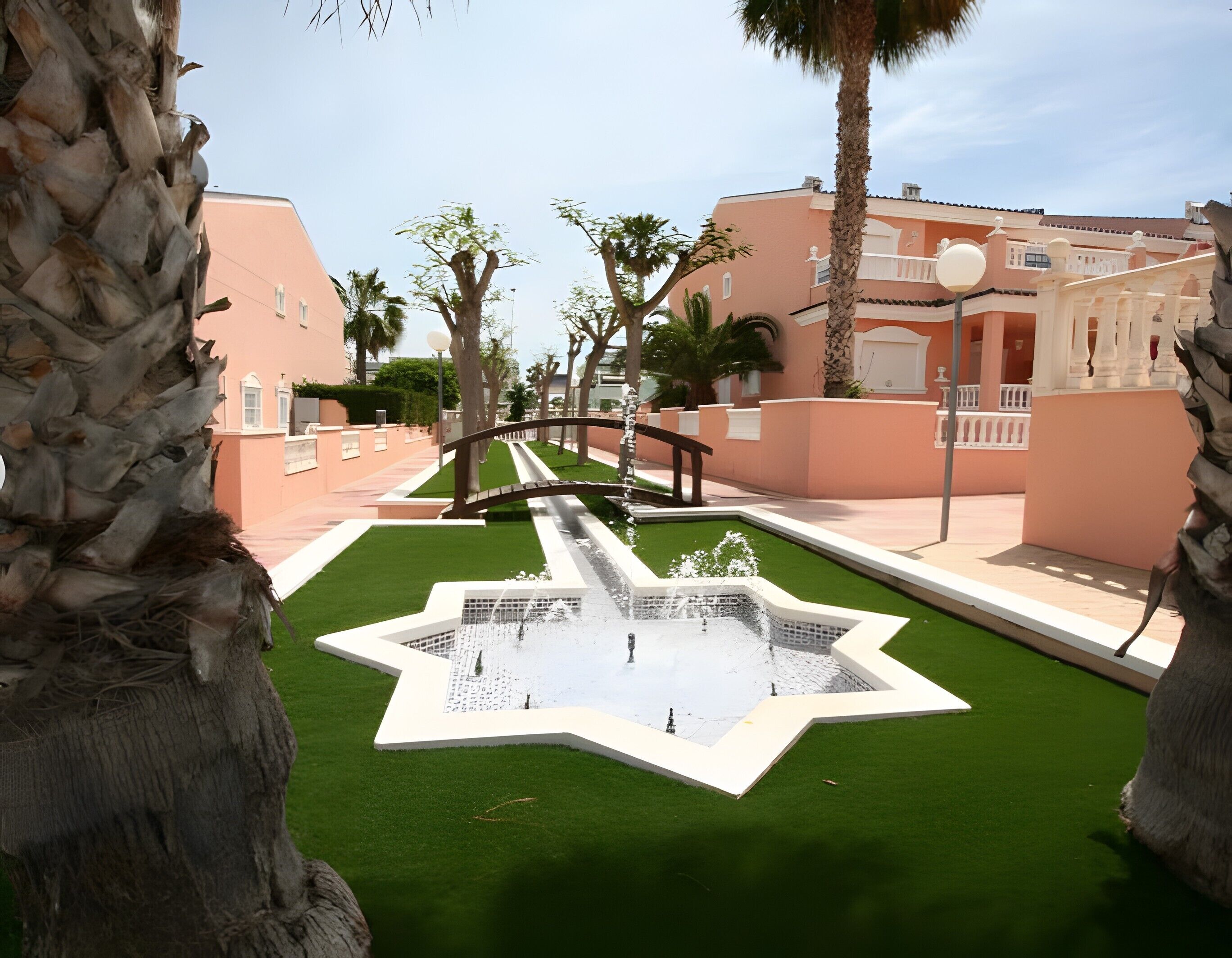 A landscaped area with a fountain, palm trees, and buildings with balconies.