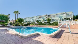 Ein Schwimmbecken mit einer gefliesten Terrasse, umgeben von einem Gebäude mit Balkonen und blauem Himmel.
