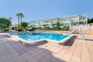 A swimming pool with a tiled deck, surrounded by a building with balconies and a clear sky. - Bungalow 'Magnifico Chalet Con Piscina' with Shared Pool, Wi-Fi and Air Conditioning (Gran Alacant)