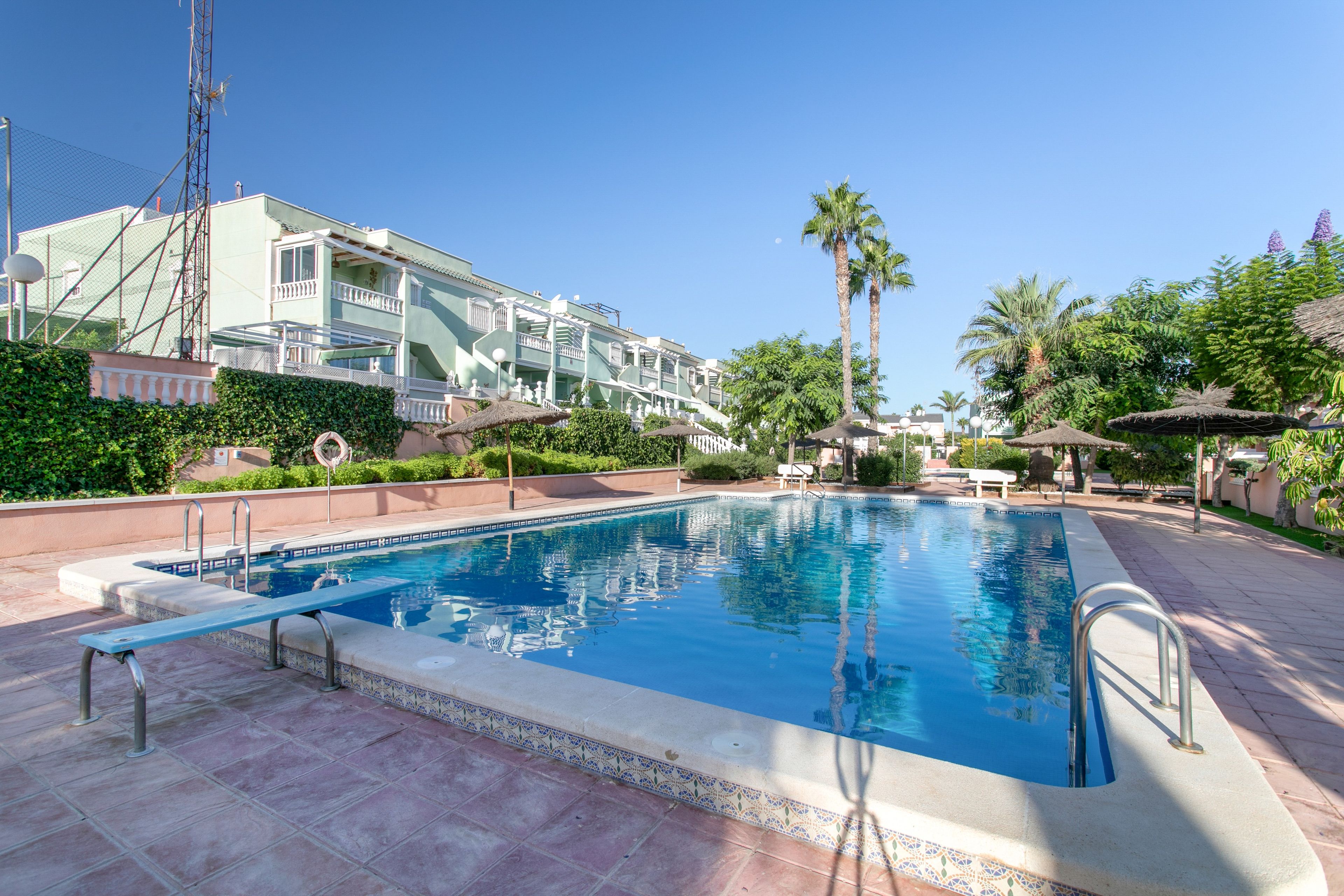 A swimming pool with a tiled edge, surrounded by a paved area with lounge chairs and umbrellas.