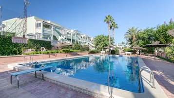 A swimming pool with a tiled edge, surrounded by a paved area with lounge chairs and umbrellas.