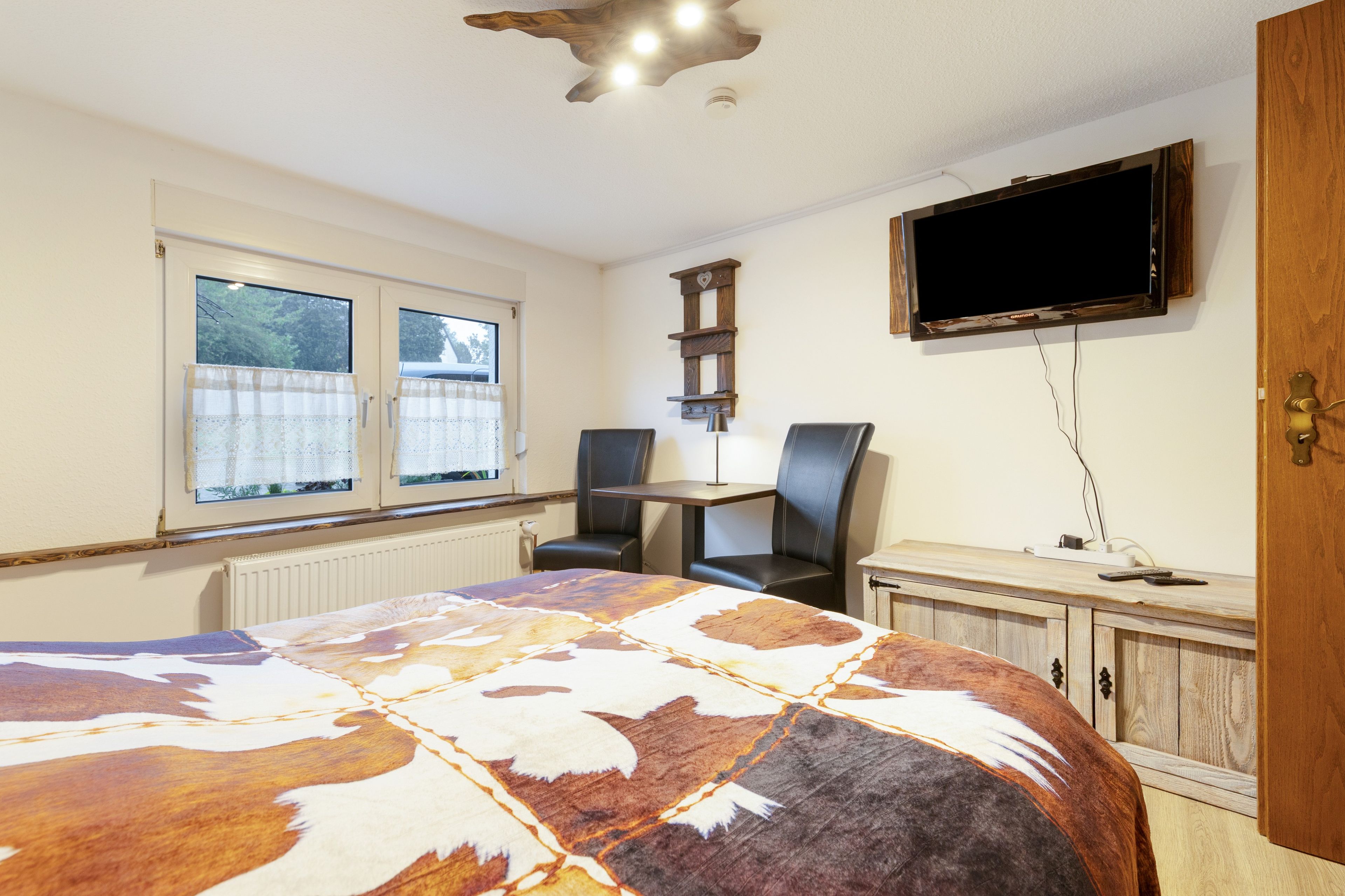 A bedroom with a bed, two chairs, a television, and a desk.