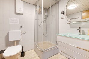 A modern bathroom with a glass-enclosed shower, a white toilet, and a glass sink.