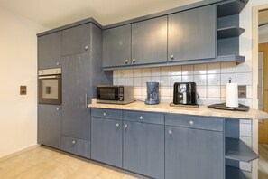 A modern kitchen with grey cabinets, a built-in oven, a microwave, a coffee maker, and a paper towel holder.