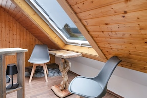 A small, sloped-roofed room with wooden walls, a table, two chairs, and a unique wooden table base.