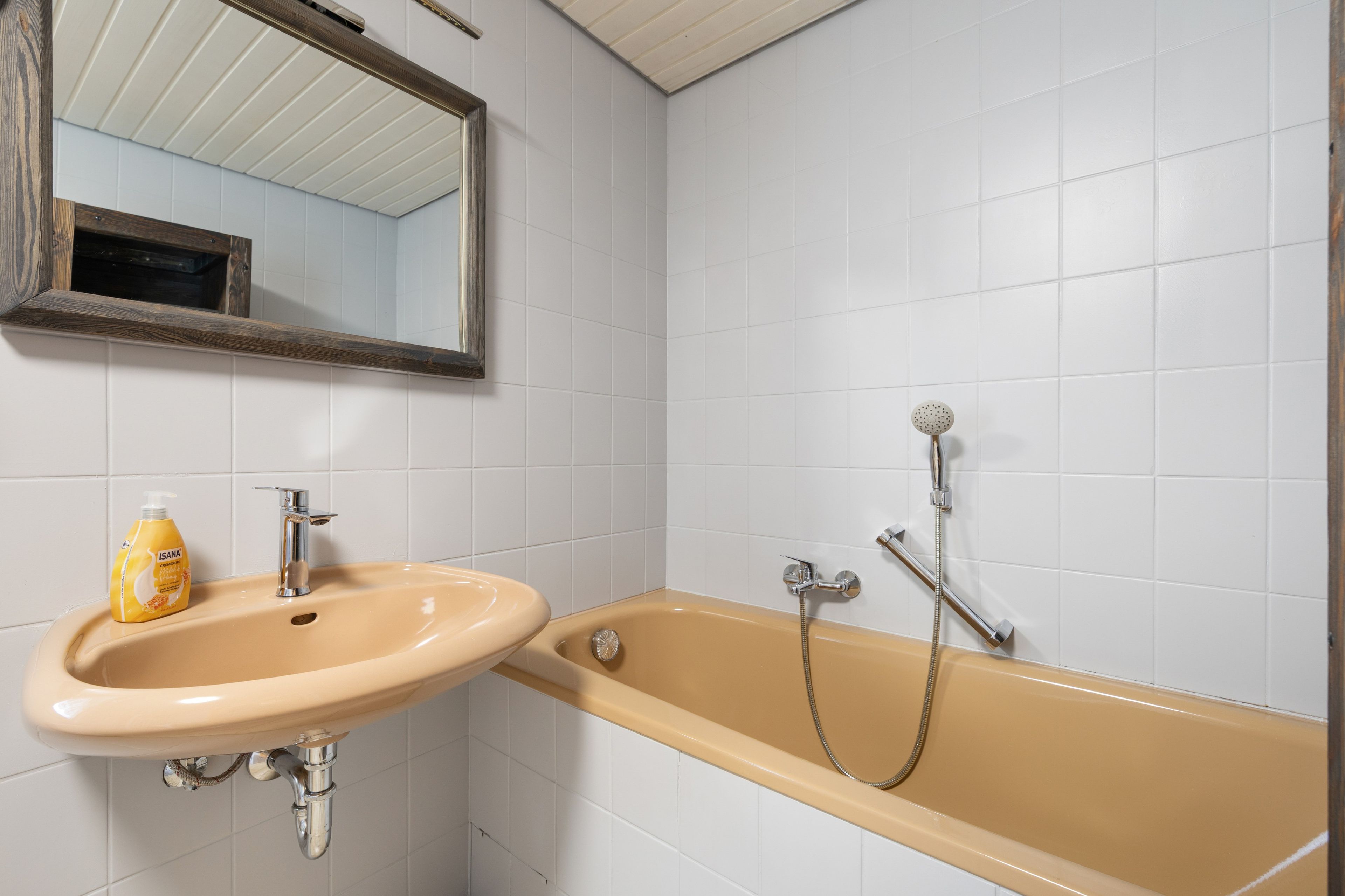 A bathroom with a beige sink, a mirror, and a bathtub with a showerhead.
