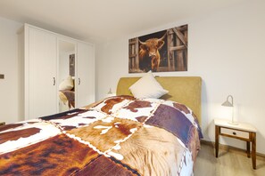 A bedroom with a bed, a nightstand, a lamp, a wardrobe, and a painting of a cow.