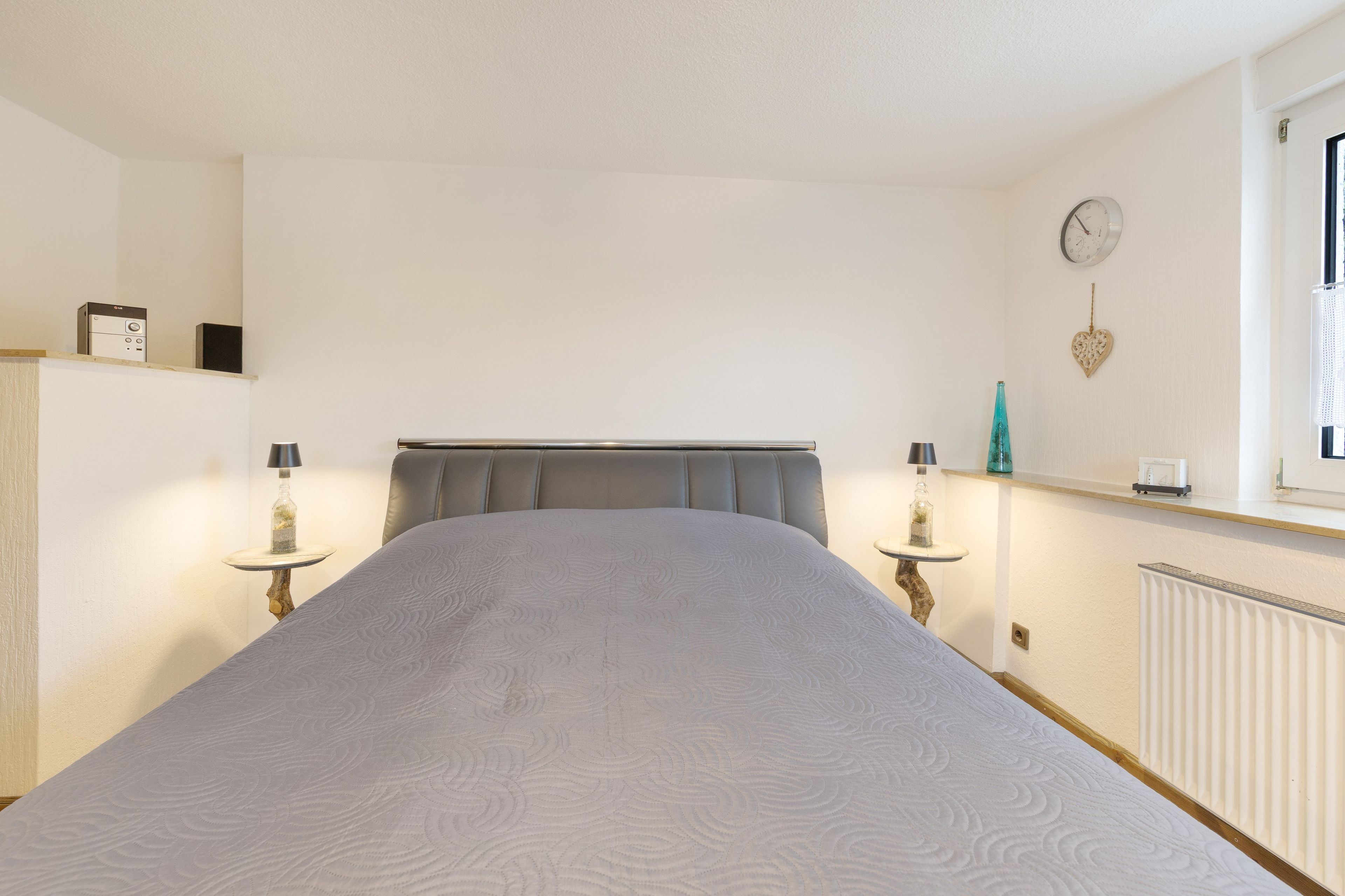 Ein Schlafzimmer mit einem Bett, Nachttischen, einer Uhr und einem Fenster.