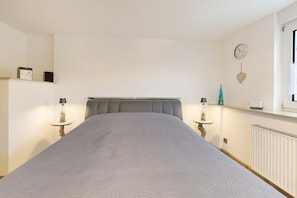 Un dormitorio con una cama, mesitas de noche, un reloj y una ventana.