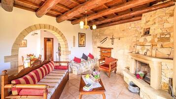 A rustic interior with a wooden ceiling, stone walls, a fireplace, a sofa, and a dining area.