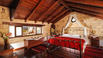 A room with a wooden ceiling, stone walls, a bed with a red bedspread, a wooden dresser, and a window with a view.