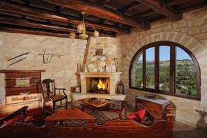 A rustic room with a stone fireplace, wooden furniture, and a view through a large arched window. - Villa for 2-4 Adults – Two Floors, Mountain View, Wi-Fi, Air Conditioning (Sellia)