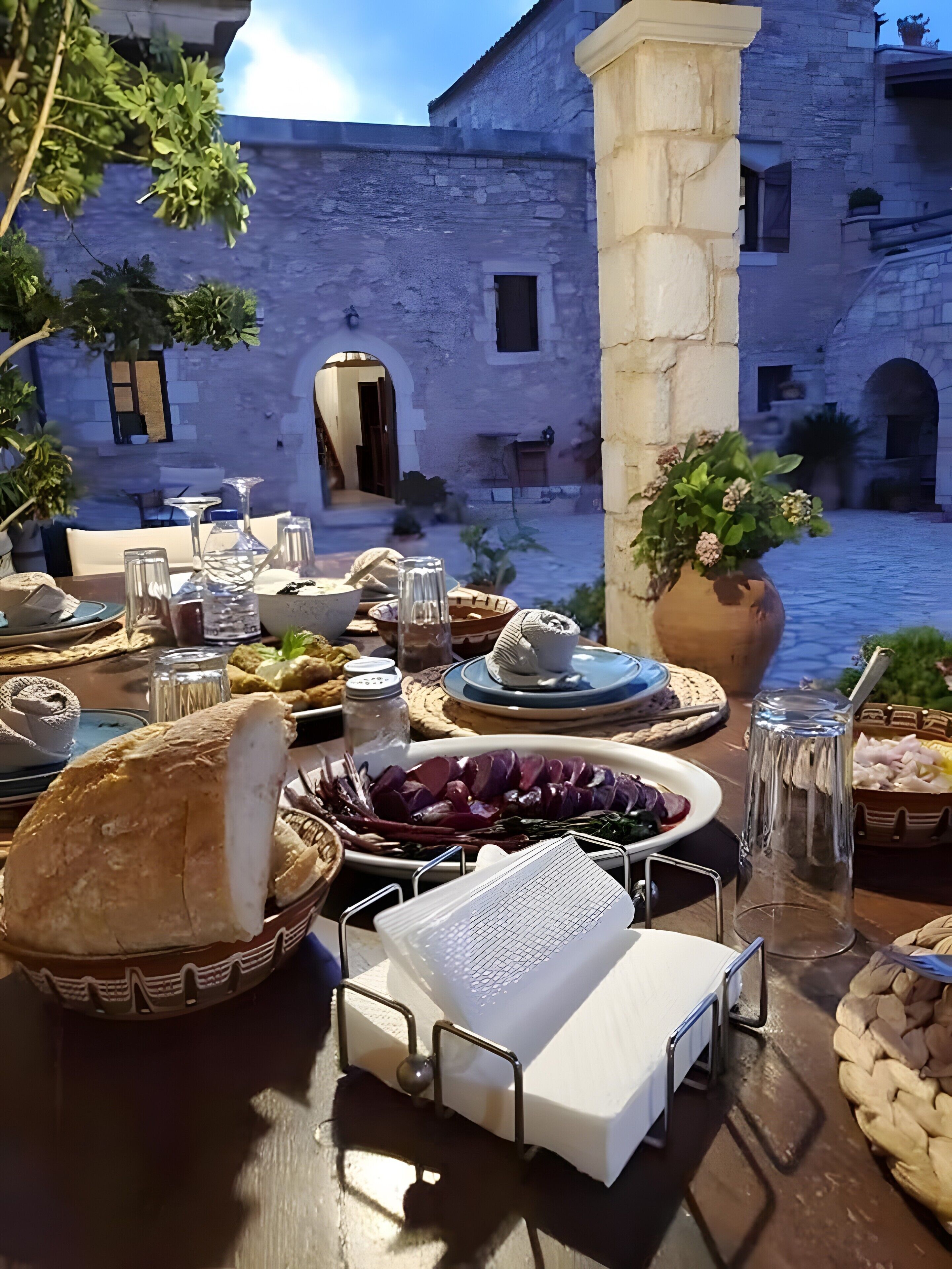 An outdoor dining area with stone walls, a table set with food and drink, and a view of a courtyard.