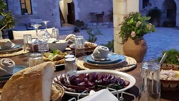 An outdoor dining area with stone walls, a table set with food and drink, and a view of a courtyard.