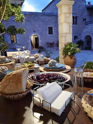 An outdoor dining area with stone walls, a table set with food and drink, and a view of a courtyard.