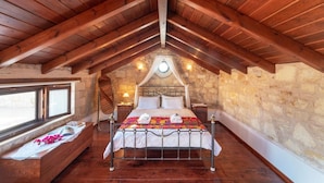 A bedroom with a stone wall, a wooden ceiling, a bed with a canopy, a bedside table, and a window.