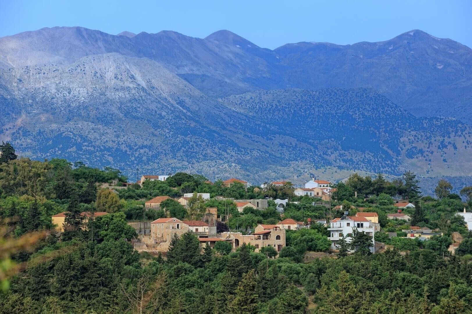 A mountainous landscape with a cluster of buildings surrounded by dense greenery.