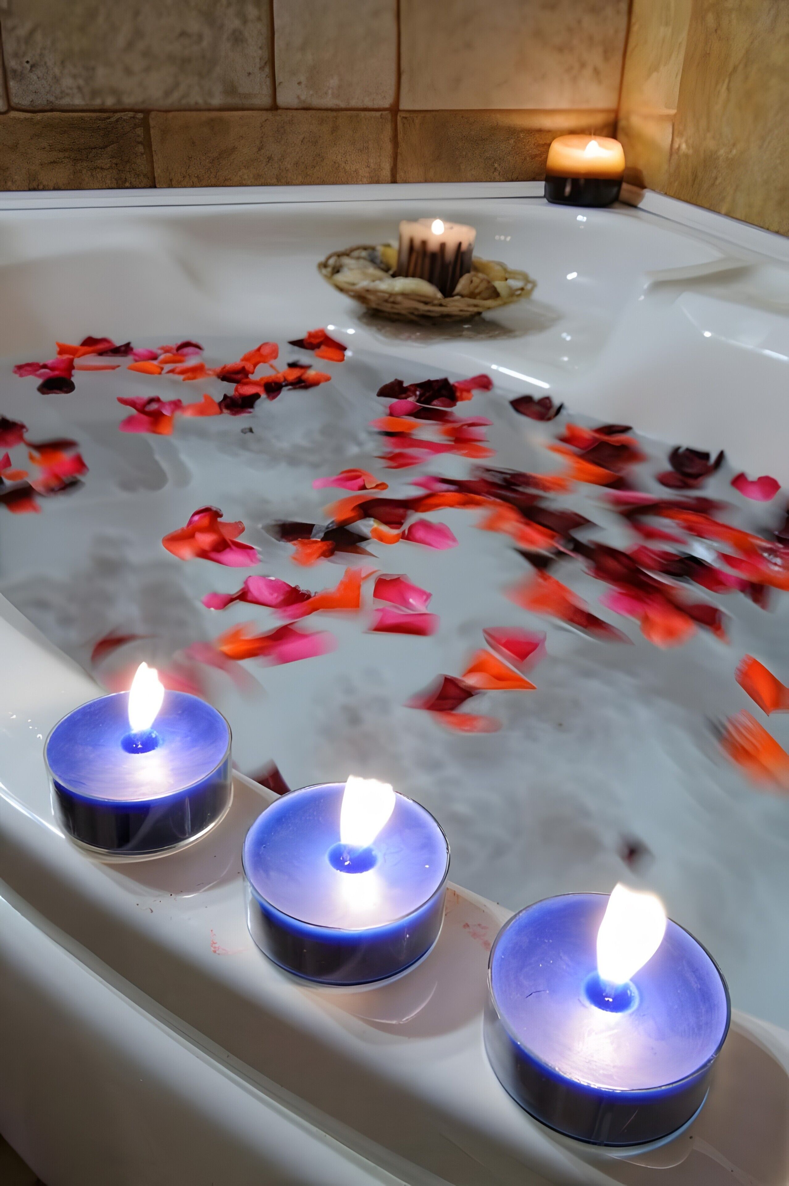 Una bañera con tres velas encendidas y pétalos de rosa flotando en el agua.