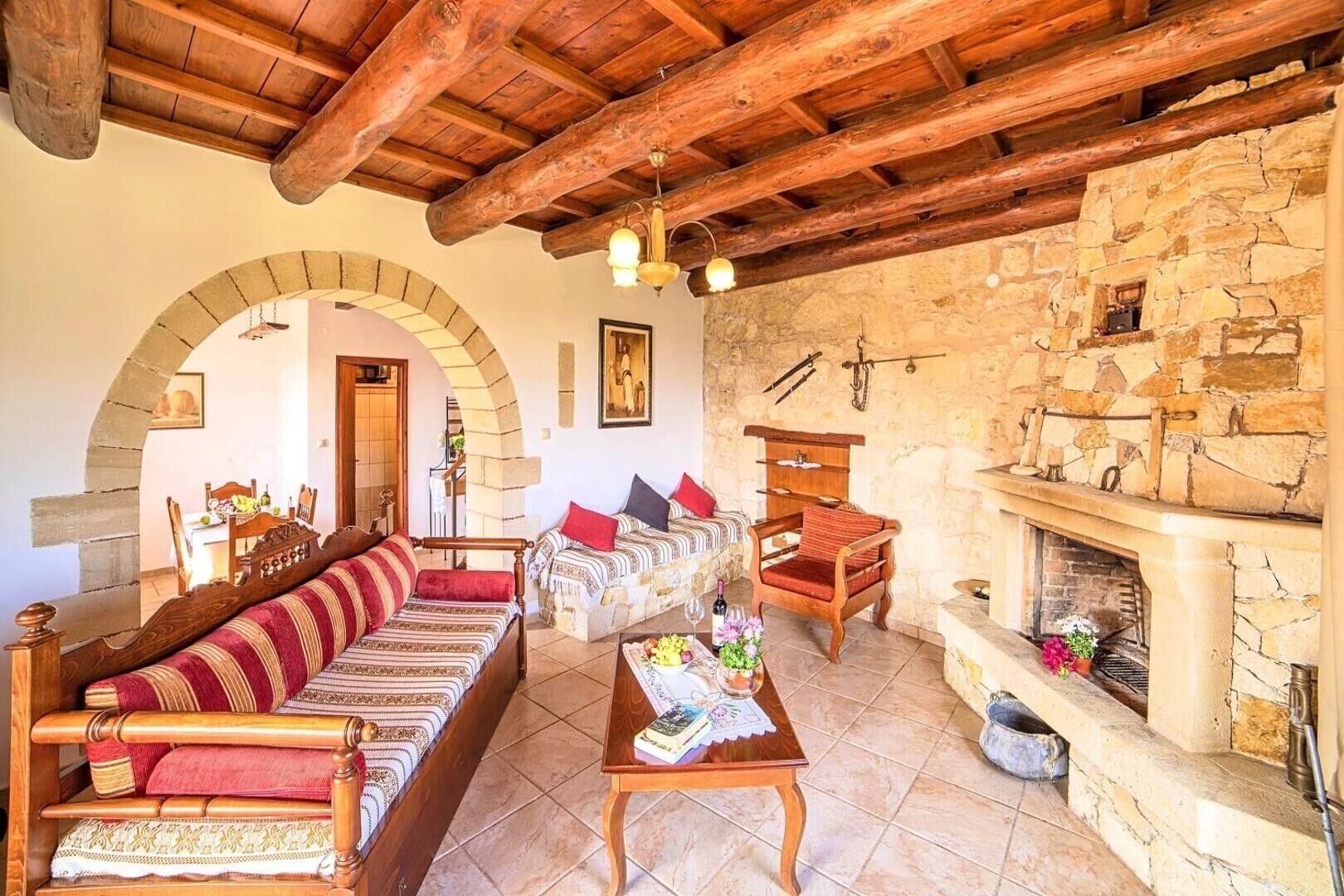A rustic interior with a wooden ceiling, stone walls, a fireplace, a sofa, and a dining area.