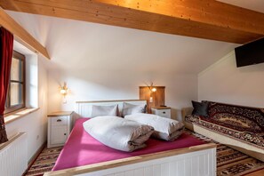 Un dormitorio con cama, mesitas de noche, sofá, ventana y televisor instalado en la pared.