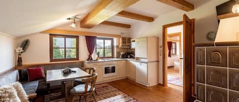 Una cocina acogedora con vigas de madera, un comedor con mesa y sillas, y vistas al exterior a través de amplios ventanales.
