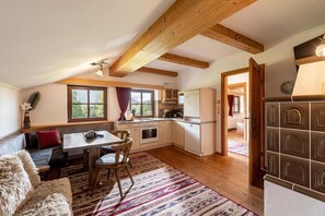 Eine gemütliche Küche mit Holzbalken, einem Essbereich mit Tisch und Stühlen und Blick ins Freie durch große Fenster.