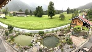 Un paisaje rural con un estanque, una casa de madera y un campo cercado.