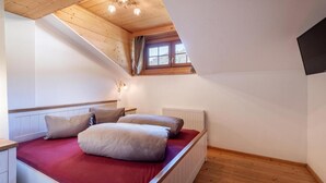 Un dormitorio con techo inclinado, una ventana con cortinas, una cama con almohadas y un radiador.