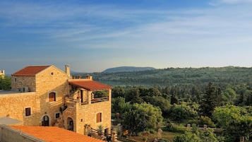 Un edificio in pietra con tetto in tegole rosse, un balcone e vista su un pendio boscoso.