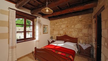 A bedroom with a stone wall, a wooden bed, a window with curtains, and a wooden ceiling.