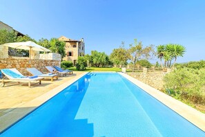 Un espace aménagé au bord de la piscine, avec des chaises longues et un bâtiment en pierre en arrière-plan.