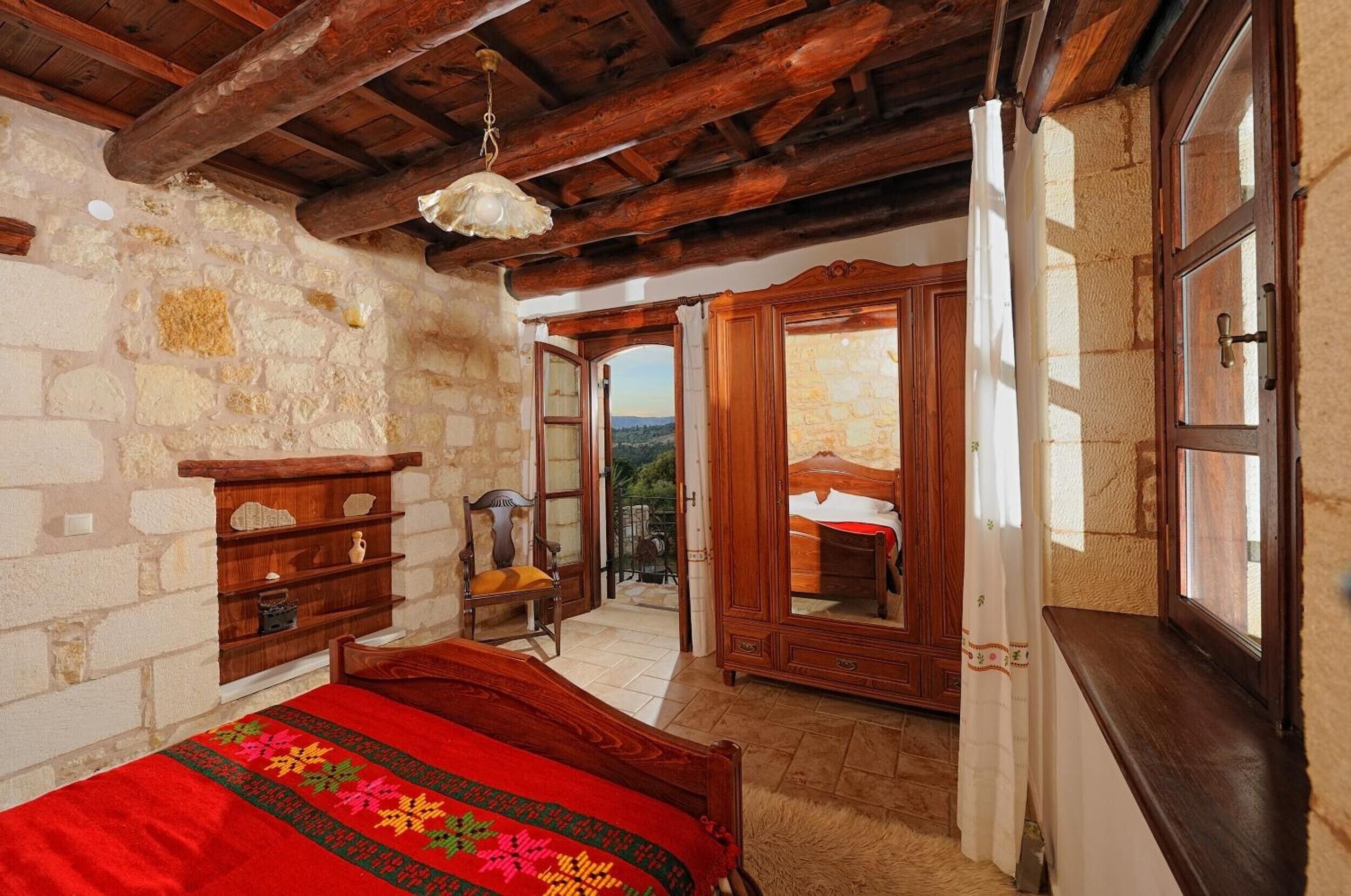 A bedroom with a wooden bed, a stone wall, a wooden chair, and a view through an open door.