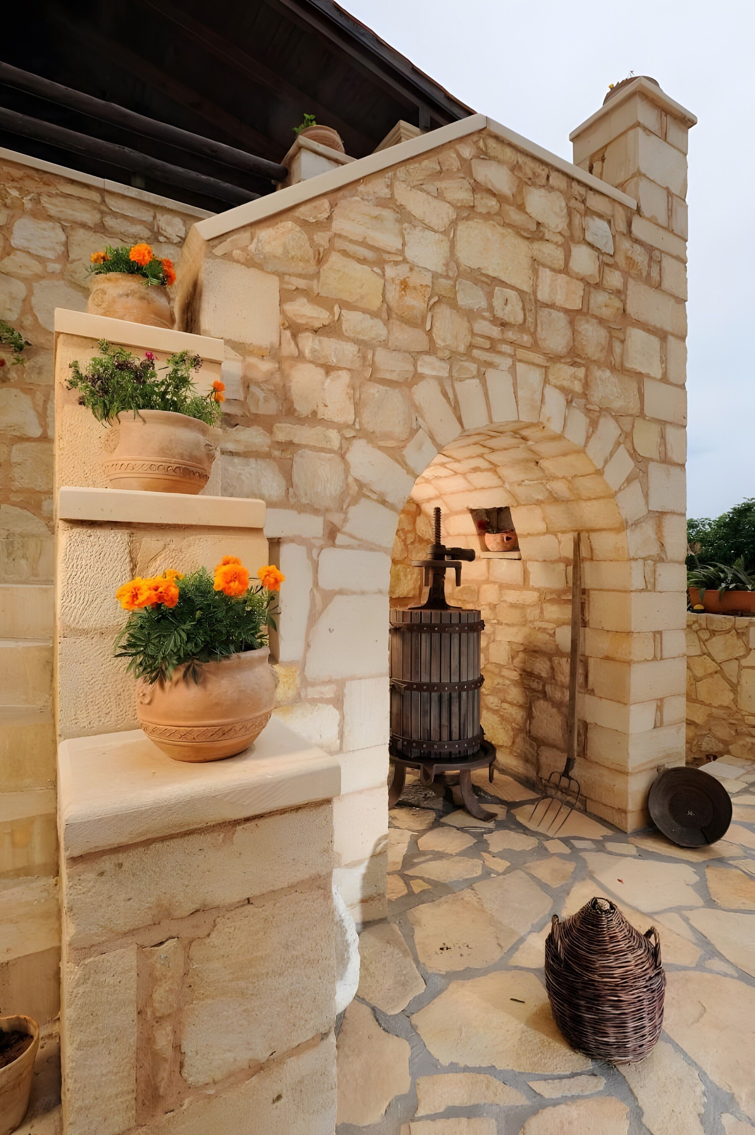 Un edificio in pietra con un ingresso ad arco, piante in vaso e un cesto di vimini sul terreno.