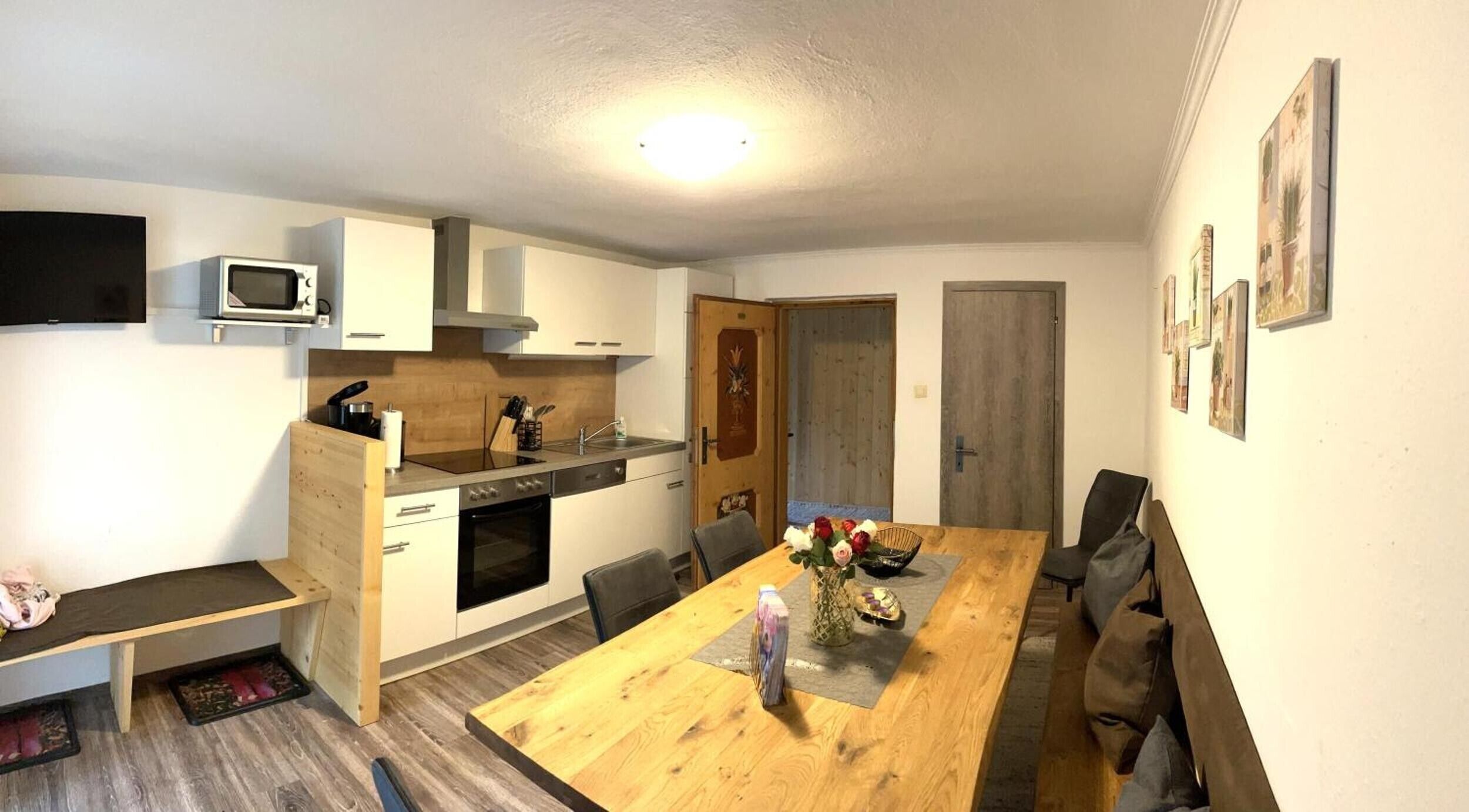 A compact kitchen with a microwave, stove, and sink. There is a dining table with chairs and a bench.