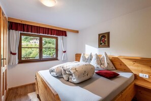 Ein Schlafzimmer mit Holz-Kopfteil, einem Bett mit Blumenbettwäsche, einem Fenster mit Vorhängen und einem Bild an der Wand.