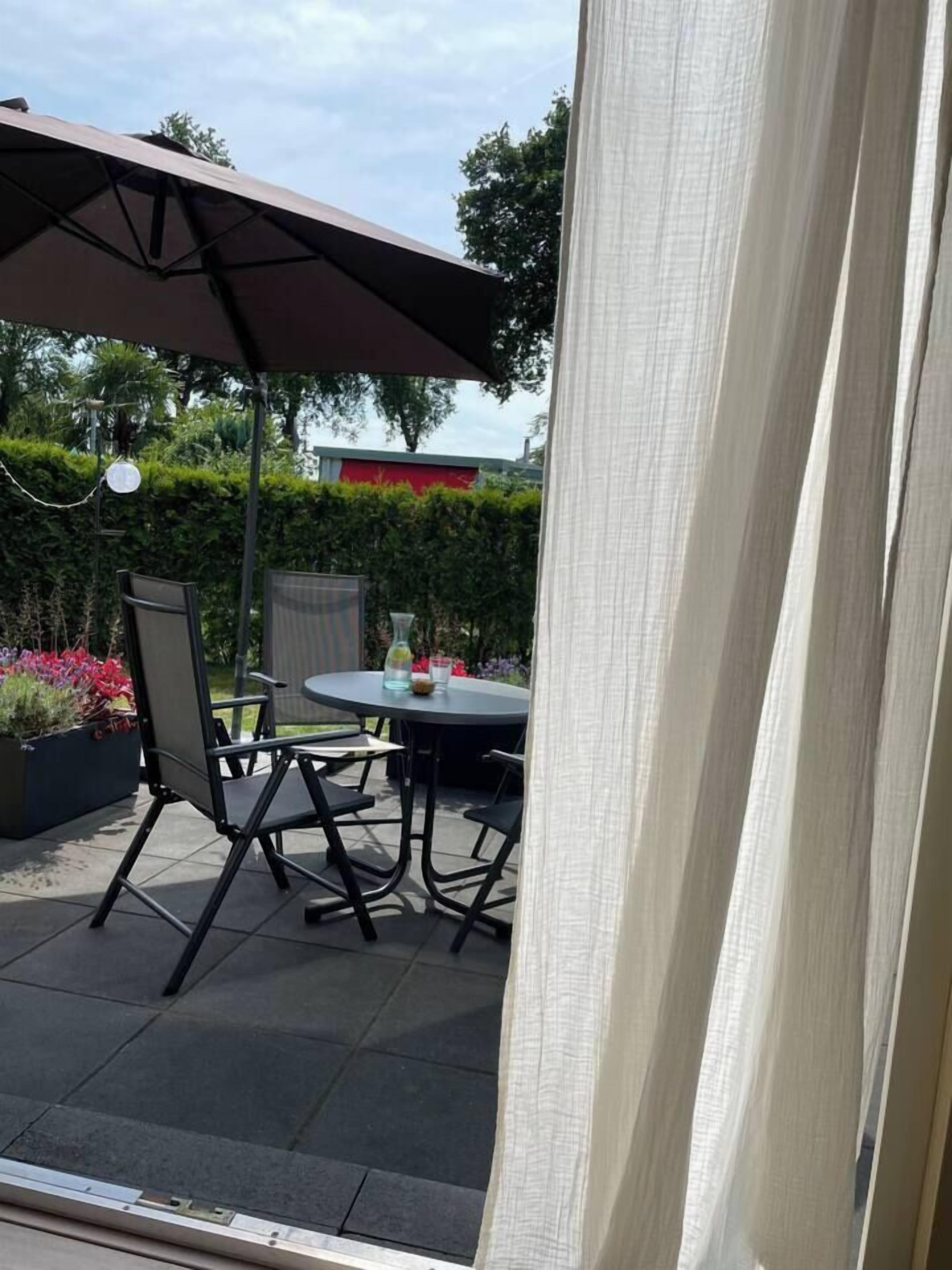 An outdoor patio with a round table and chairs, a large umbrella, and a potted plant.