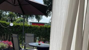 An outdoor patio with a round table and chairs, a large umbrella, and a potted plant.