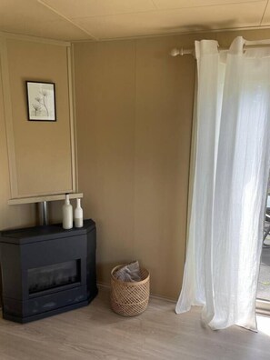 Une pièce avec une cheminée, un tableau encadré au mur, un panier et un rideau blanc.