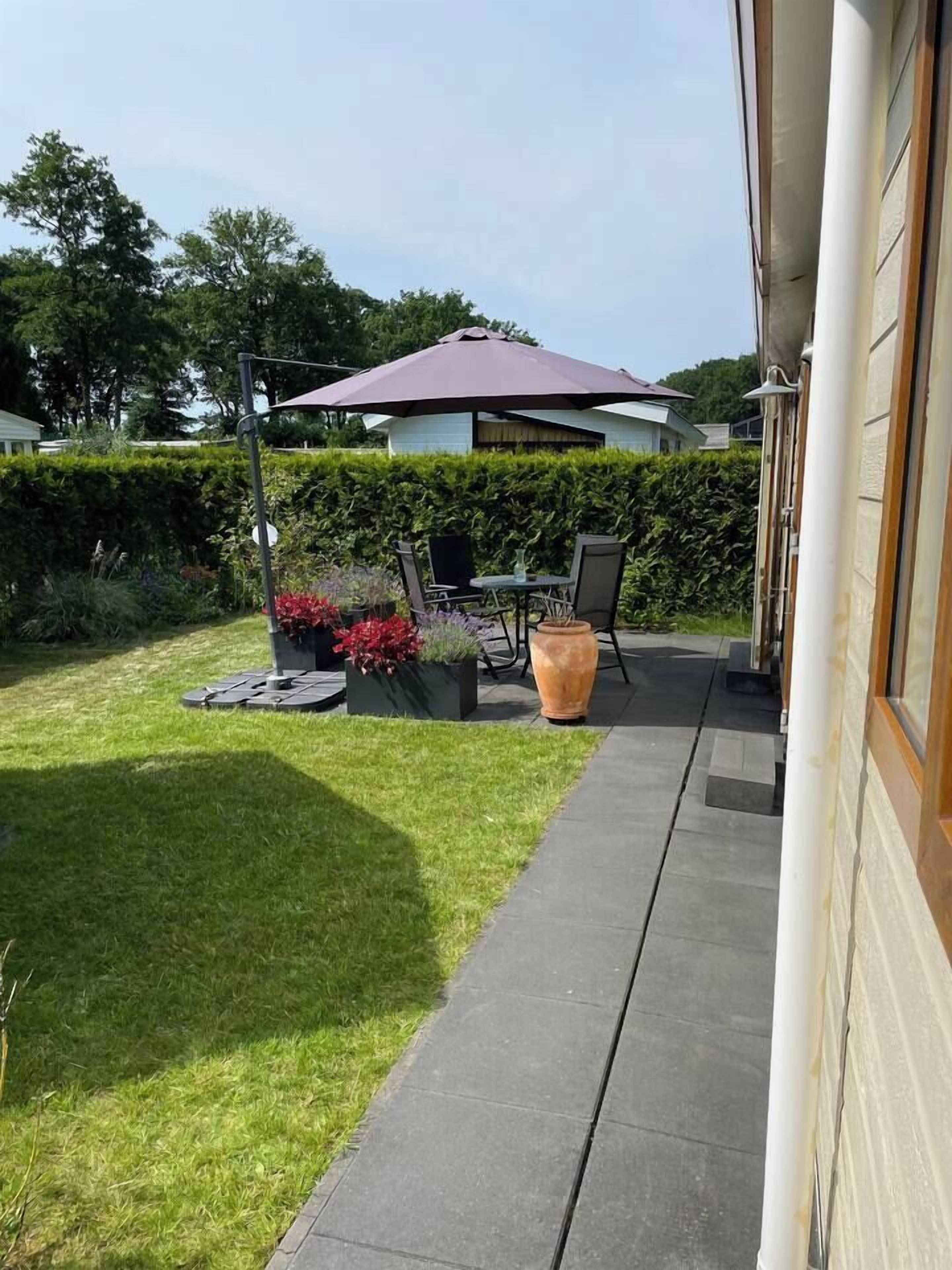 Een terras met een tafel, stoelen, een grote parasol en potplanten.