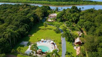 Vista aérea de um resort com piscina, palmeiras e um rio.