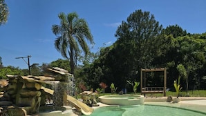 A clear pool with a waterfall feature, surrounded by rocks and greenery.