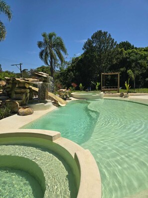 A clear pool with a waterfall feature, surrounded by rocks and greenery.