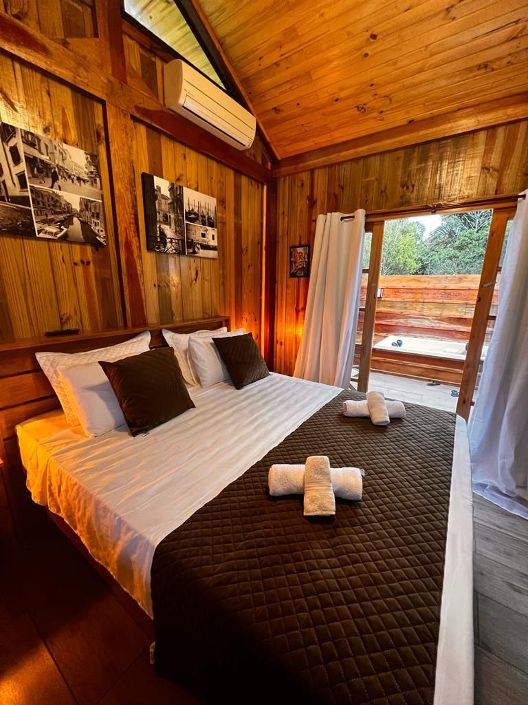 Quarto de madeira com cama, fotografias nas paredes e vista pela janela.