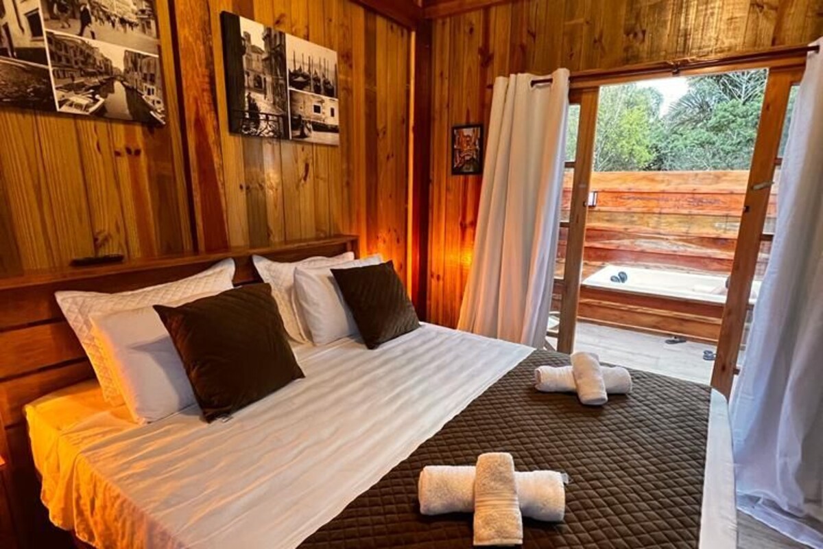 A wooden room with a bed, photographs on the wall, and a view through a window.